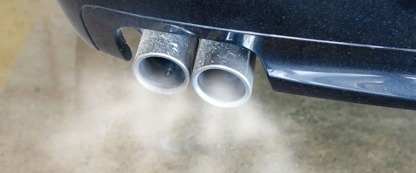 Doble salida de escape de un coche echando humo sobre el asfalto