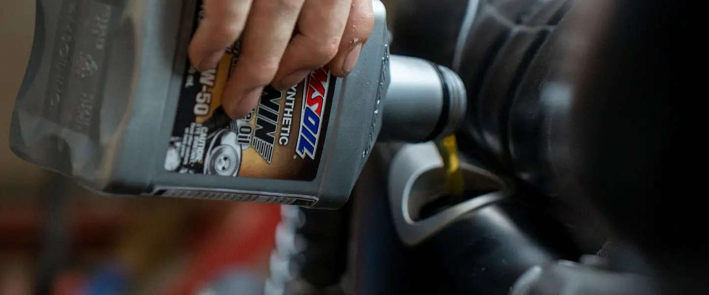 Persona vertiendo aceite de motor nuevo en el motor de una moto, en un garaje