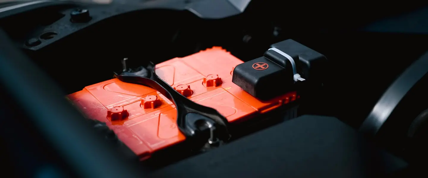 Batería de coche naranja instalada en el vano motor, con la pletina de sujeción y el capuchón del borne positivo